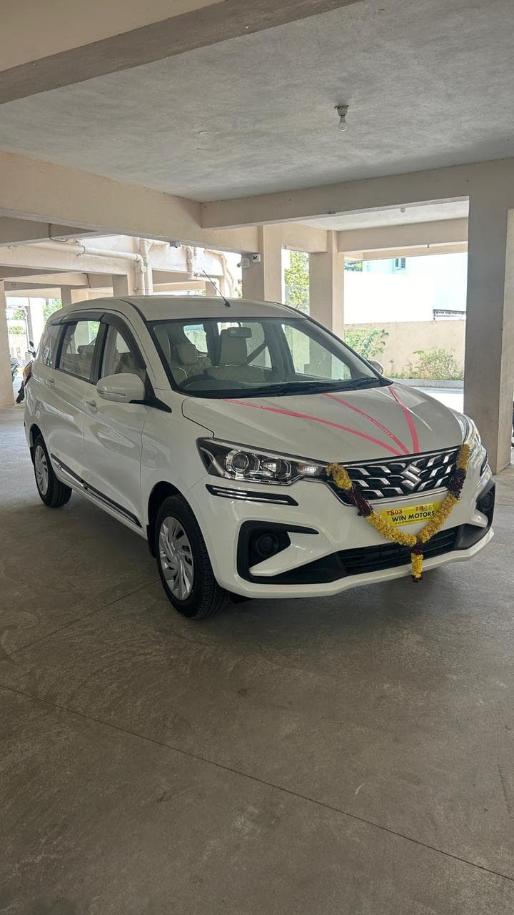 A photo of a Maruti Ertiga VXI 2026 - White MUV with garland.